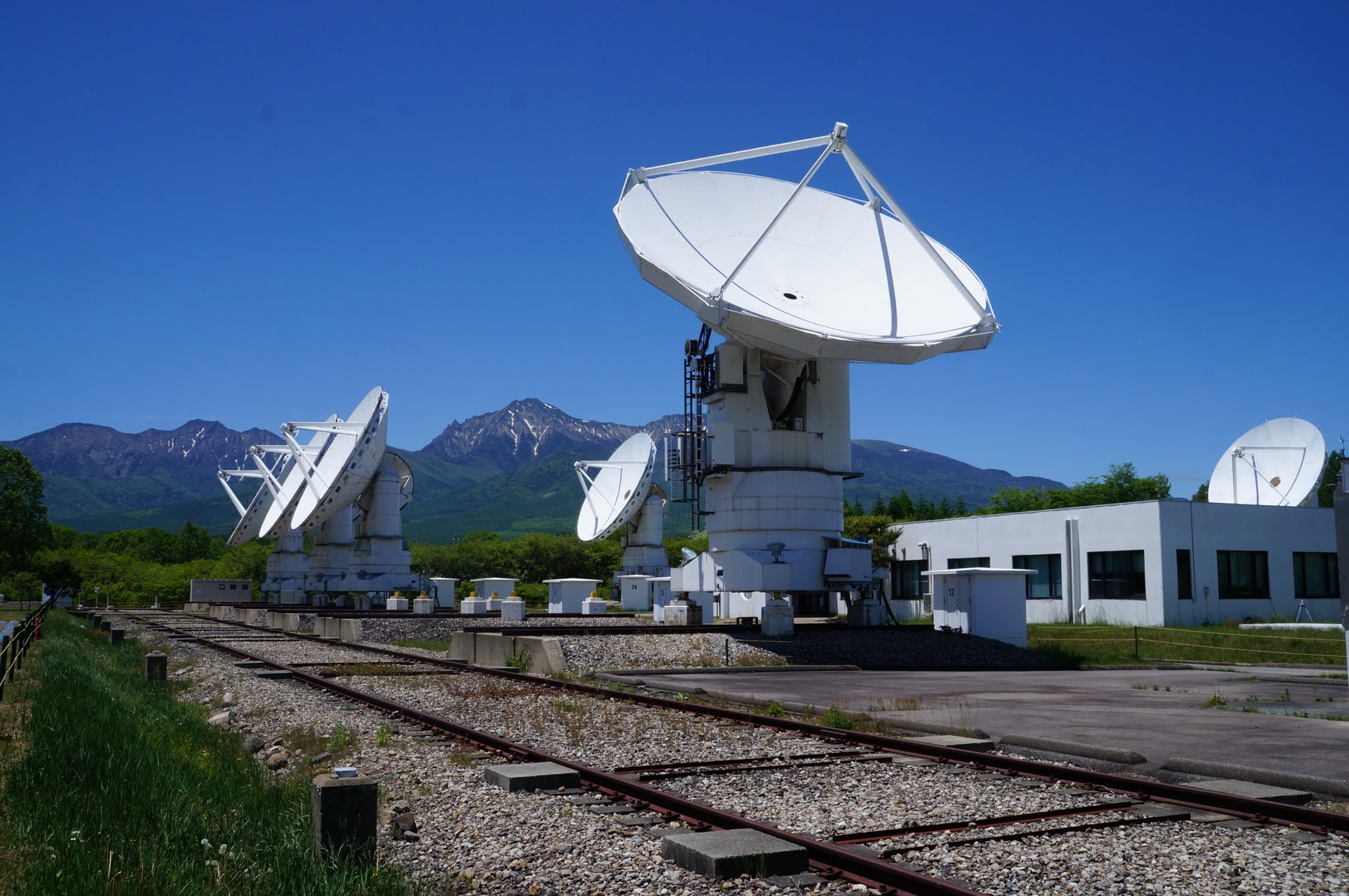 Four radio telescope dishes on tracks with a mountain backdrop.